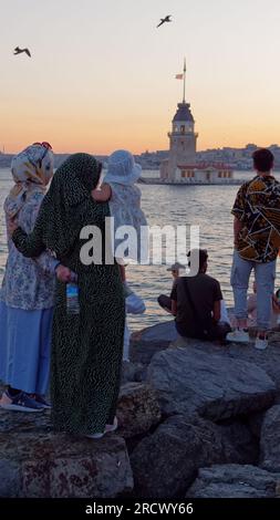 Zwei Frauen mit einem Kind stehen auf Felsen und genießen den Sommeruntergang über dem Bosporus-Meer und dem Maidens-Turm von Uskudar, Istanbul, Türkei Stockfoto