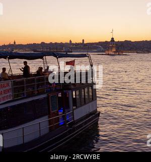 Menschen auf einem Boot genießen den Sonnenuntergang über dem Bosporus Meer und dem Maidens Tower von Uskudar, Istanbul, Türkei. Kreuzfahrtschiff hinten. Stockfoto