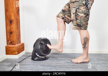 Mann, der die Füße auf dem Ventilator kühlt und auf dem Boden steht Stockfoto