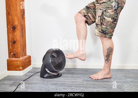 Mann, der die Füße auf dem Ventilator kühlt und auf dem Boden steht Stockfoto