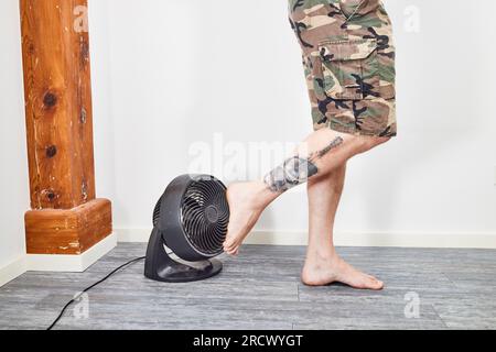 Mann, der die Füße auf dem Ventilator kühlt und auf dem Boden steht Stockfoto