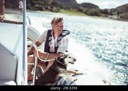 Der Rentner sitzt und lächelt mit dem Hund auf dem Schnellboot Stockfoto