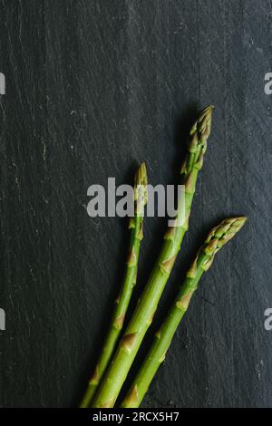 Drei Spargelspieße lagen auf einer schwarzen Schieferplatte Stockfoto