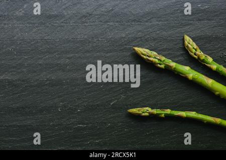 Nahaufnahme von drei Spargelspitzen auf schwarzem Schiefer Stockfoto