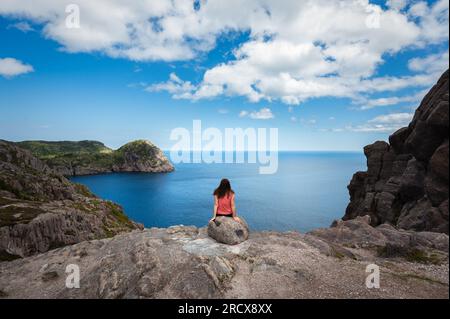 Frau sitzt auf einem Felsen mit Blick auf das Meer in St. John's, Neufundland. Stockfoto