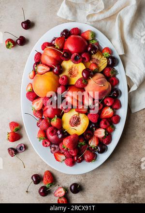 Blick von oben auf eine große Platte mit gemischten Früchten: Beeren, Pfirsiche, Kirschen. Stockfoto