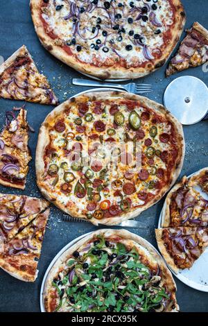 Pizza-Abendessen. Flache Unterlage mit verschiedenen Arten italienischer Pizza auf rustikalem Tisch, Draufsicht. Schnelles Mittagessen, Feiern, Tagungskonzept. Vertikales Foto Stockfoto