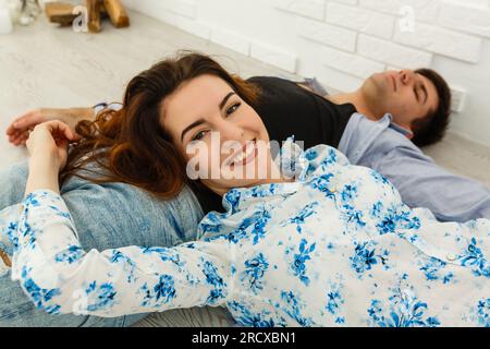 Ein traumhaftes Paar, das auf dem Boden liegt, in einem leeren Raum liegt und aufblickt. Stellen Sie sich ein zukünftiges Innenraumprojekt vor, weißer Hintergrund. Stockfoto