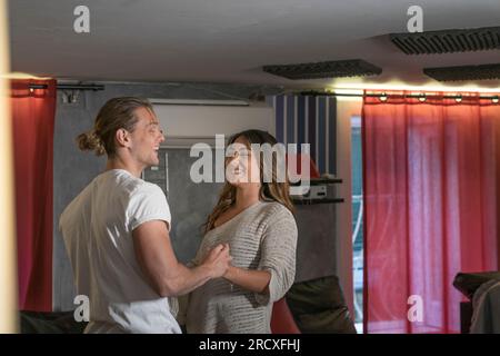 Ein Paar im Haus, das im Wohnzimmer tanzt und Spaß hat, lächelt und lautstark - Gelbes und blaues Licht. Liebhaber haben beim Flirten den Ball gedreht Stockfoto