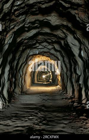 Ein alter dunkler Tunnel im Fels. Licht am Ende des Tunnels. Vertikales Foto Stockfoto