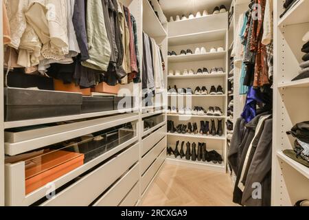 Ein begehbarer Kleiderschrank mit weißen Regalen und vielen Kleidern, die dahinter an der Wand hängen, Stockfoto