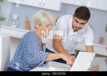 youngerman hilft einem älteren Menschen mit einem Laptop Stockfoto