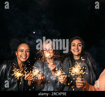 Drei glückliche Frauen mit Glitzer. Eine Gruppe verschiedener weiblicher Freunde bei Nacht. Stockfoto