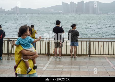 Die Leute wagen sich raus und spüren die Macht des Taifuns Talim in Heng Fa Chuen. In den frühen Stunden des 17. Juli, als sich der Taifun Talim Hongkong nähert, gibt das Hong Kong Observatory um 12:40 Uhr morgens das Warnsignal für den Taifun Nr. 8 aus Dieses Signal ruft in der ganzen Stadt erhebliche Veränderungen hervor, wobei die meisten Busverbindungen zum Stillstand kommen und die Börse als Reaktion auf die unmittelbare Gefahr ihre Türen schließt. Inmitten dieser Vorsichtsmaßnahmen bietet die MTR (Mass Transit Railway) jedoch weiterhin begrenzte U-Bahn-Dienste an, um sicherzustellen, dass Anwohner und Reisende über ein Transportmittel verfügen Stockfoto