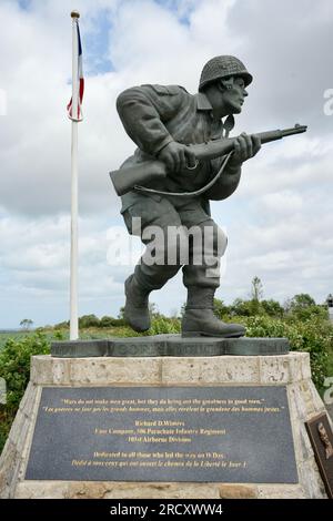 Denkmal für Major Richard D Winters und Easy Company, mit US- und französischen Flaggen und Landschaft dahinter. Utah Beach, Frankreich, 3. Juli 2023. Stockfoto