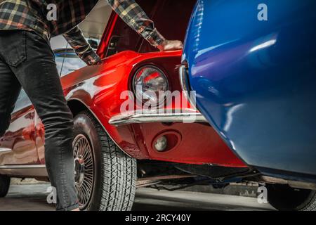 Ein Weißer Mann, Der Unter Der Motorhaube Eines Klassischen Muscle Car Nach Potenziellen Motorproblemen Sucht Stockfoto