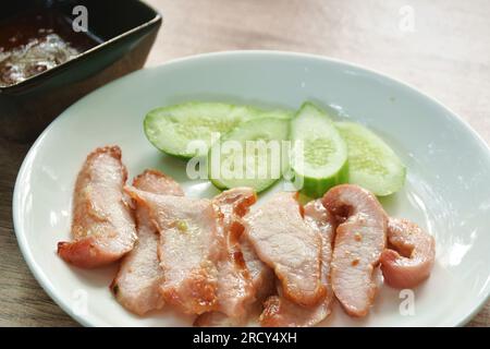Gegrillter Schweinehals mit einer Gurke auf dem Teller, die würzige Sauce eintaucht Stockfoto