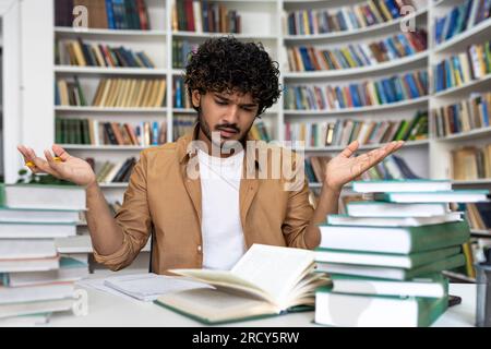 Unzufriedener und frustrierter Student, der sich auf die Prüfung selbst konzentrieren und sich auf sie vorbereiten wollte, Mann, der in der Bibliothek saß, ermüdet, nur schwer zu lernen und Material zu lernen. Stockfoto
