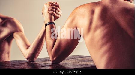 Die Hände zweier Männer umklammerten Arm-Wrestling, stark und schwach, ungleiche Übereinstimmung. Armdrücken. Kräftig muskeliger, bärtiger Arm, der mit einem schwachen Mann kämpft Stockfoto