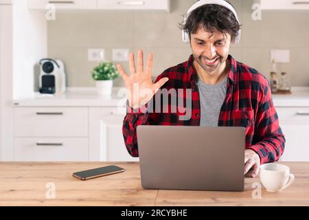 Lächelnder männlicher Student, der sich während eines Videogesprächs zu Hause mit der Hand winkte Stockfoto