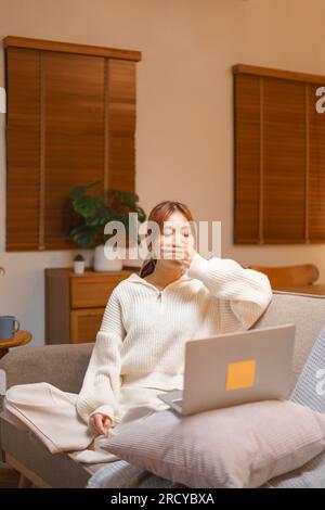 Konzept des Nachtlebens, Junge Frau schläfrig und gähnend, während sie spät nachts im Winter an einem Notebook arbeitet. Stockfoto