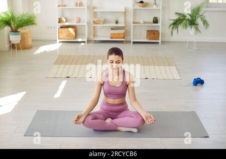 Eine friedliche, sportliche junge Frau, die zu Hause Yoga macht und in Lotus-Pose sitzt. Stockfoto