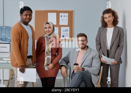 Eine Gruppe junger erfolgreicher Mitarbeiter mit Finanzdokumenten, die vor der Kamera stehen, gegen ein Plakat mit Papieren stehen und Sie ansehen Stockfoto