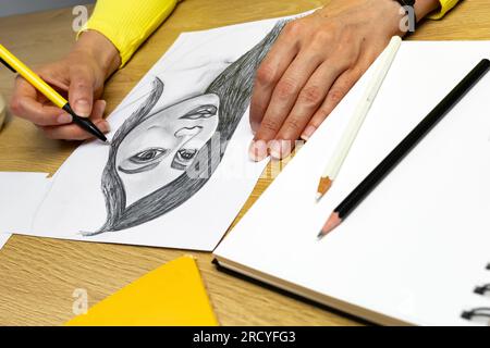 Der Künstler zeichnet ein Porträt einer Frau mit einem Bleistift auf weißem Papier. Stockfoto