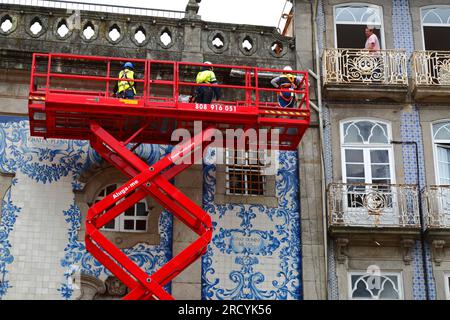 Ein Mann auf dem Balkon beobachtete Arbeiter auf einer erhöhten Scherenaufzugplattform bei der Wartungsinspektion der Igreja do Carmo Kirche, Porto/Porto, Portugal Stockfoto