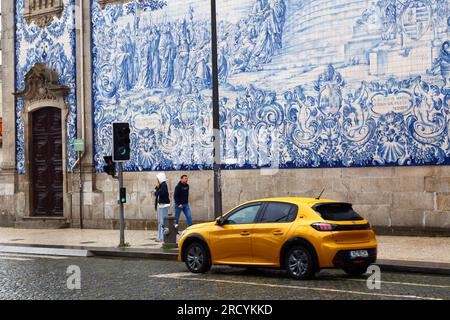 Gelbes Auto, das an den Asulejos/Keramikfliesen an der Seitenwand der Kirche Igreja do Carmo, Porto/Porto, Portugal vorbeifährt Stockfoto