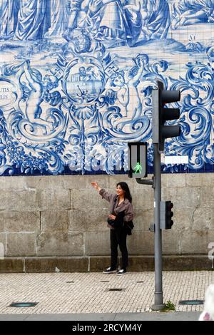 Eine junge asiatische Touristin posiert für ein Foto vor den Asulejos/Keramikfliesen an der Seitenwand der Kirche Igreja do Carmo, Porto/Porto, Po Stockfoto