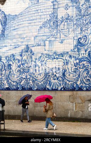 Touristen mit Schirmen, die an den Asulejos/Keramikfliesen an der Seitenwand der Kirche Igreja do Carmo, Porto/Porto, Portugal vorbeilaufen Stockfoto