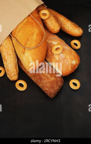 Papiertüte mit Backwaren auf einem Holztisch. Baguettes, Sesambrötchen, Long Loaf und Bagels, frischer Duft, knuspriges Gebäck Stockfoto