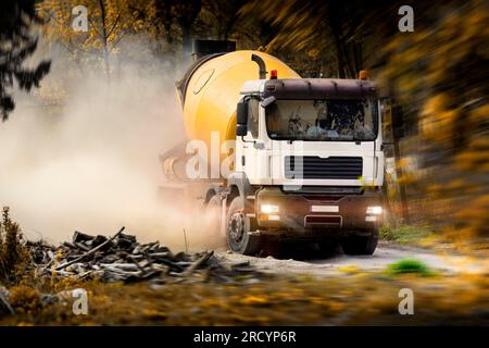 Ein Lkw, ein Betonmischer, der auf einer Schotterstraße unterwegs ist und Staubwolken in die Luft befördert. Entwicklung von Grünflächen. Städtisches Wachstum und Investitionen. Stockfoto