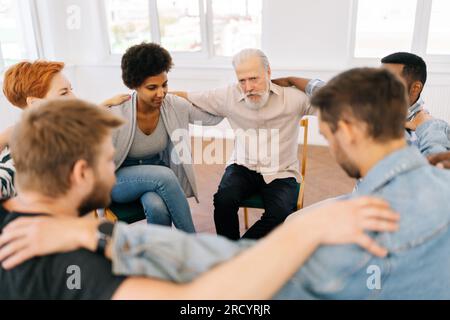 Draufsicht eines reifen männlichen Therapeuten und einer Gruppe von Mehraltern, die sich während der Gruppentherapie die Hände auf die Schultern legen Stockfoto