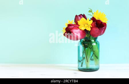 Strauß Frühlingsblumen mit Tulpen in einem Glasgefäß. Frühlingsblumen auf blauem Hintergrund. Blumen mit leerem Platz in der Nähe. Foto zum Erstellen von Postkarten Stockfoto