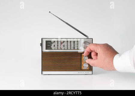 Die Hand eines Mannes dreht die Welleneinstellung. Authentisches Radio aus den 70s Jahren. Isoliert auf weißem Hintergrund. Spuren der Zeit und Spuren des Falles Stockfoto