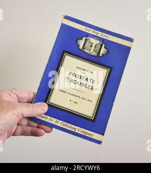 Die linke Hand eines weißen Mannes hält ein Taschenbuch „Nature Cure for Prostata Troubles“ von Harry Clements N.D. D. D. O., veröffentlicht 1964 von Health for All Stockfoto