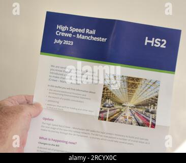 Die linke Hand eines weißen Mannes hält ein Update zum Eisenbahnprojekt HS2 High Speed Rail Crewe - Manchester, Juli 2023 Stockfoto