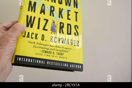 Die linke Hand eines weißen Mannes hält eine Kopie des Buches "Market Wizards" von Jack D. Schwager, den besten Händlern, von denen Sie noch nie gehört haben Stockfoto