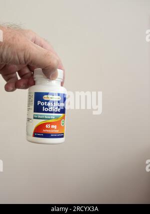 Die linke Hand eines Weißen hält einen Kunststoffbehälter mit Kaliumjodid für die kurzzeitige Anwendung, 65mg, 60 Tabletten Stockfoto