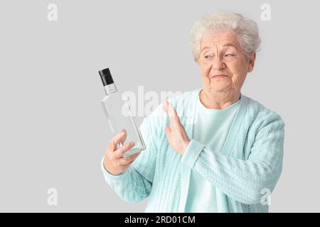 Seniorin lehnt eine Flasche Wodka auf hellem Hintergrund ab Stockfoto