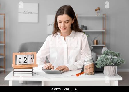 Junge Studentin, die am Tisch sitzt und ihre Finanzen kalkuliert. Studiendarlehenskonzept Stockfoto