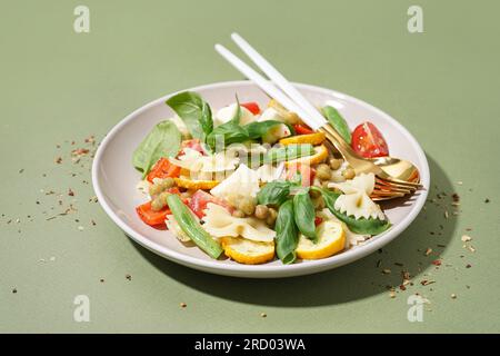 Teller mit leckerem Nudelsalat mit Erbsen und Basilikum auf grünem Hintergrund Stockfoto