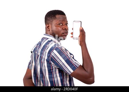 Porträt eines jungen Mannes, der auf weißem Hintergrund steht und sich mit einem Mobiltelefon in der Hand umdreht. Stockfoto