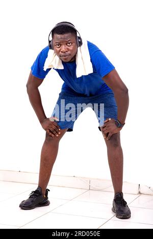 Ein junger Mann mit einem Handtuch um den Hals, der Sport im Fitnessstudio macht und Musik über Kopfhörer hört. Stockfoto