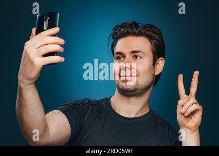 Junger Mann macht Selfie mit Siegeshandzeichen Stockfoto