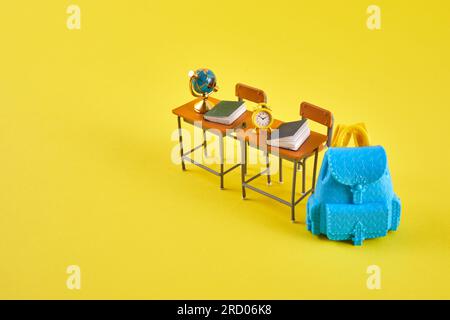 Schulschreibtisch mit Schulzubehör und blauem Rucksack auf gelbem Hintergrund Stockfoto