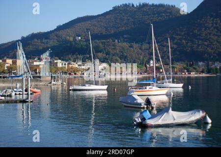 Ein atemberaubender Blick auf Boote, die auf dem Wasser des Gardasees segeln, eingerahmt von einer atemberaubenden Kulisse. Die majestätischen Berge erheben sich in der Distanz Stockfoto