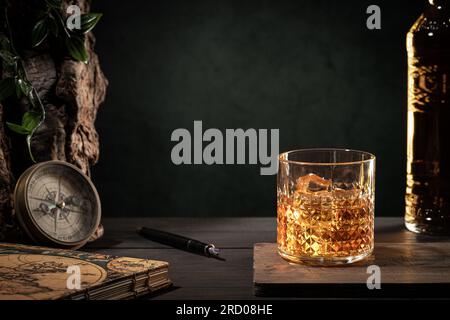Luxuriöses Leben auf einem Glas Whisky mit Eis und Flasche auf einem Holztisch auf dunklem Hintergrund mit Kopierbereich. Stockfoto